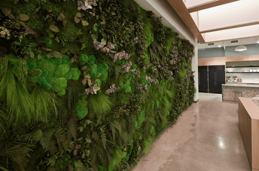 Indoor mixed green wall with preserved and artificial plants along a hallway.